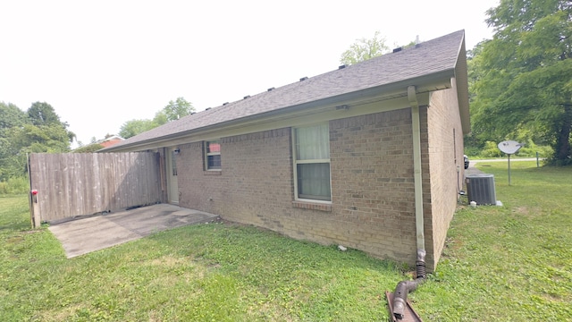rear view of property featuring cooling unit, a lawn, and brick siding