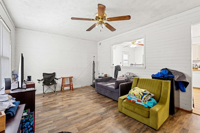 living room with wood walls, a textured ceiling, hardwood / wood-style flooring, and ceiling fan