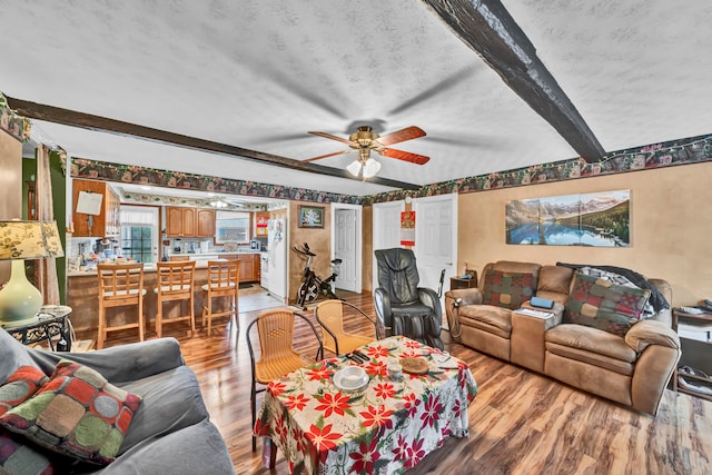 living room featuring beam ceiling, ceiling fan, and light wood-type flooring