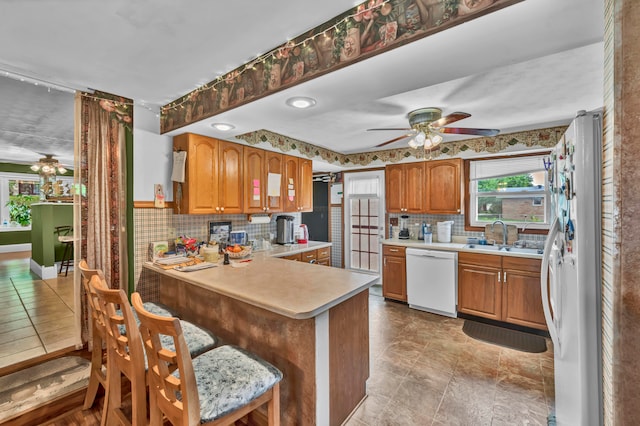 kitchen with white appliances, kitchen peninsula, light tile patterned floors, decorative backsplash, and ceiling fan