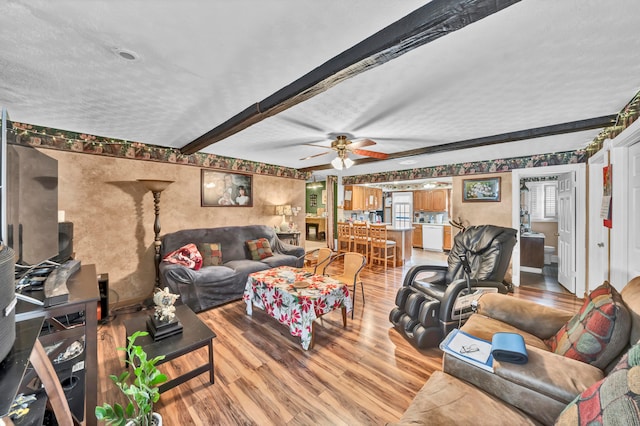 living room with a textured ceiling, light hardwood / wood-style flooring, beam ceiling, and ceiling fan