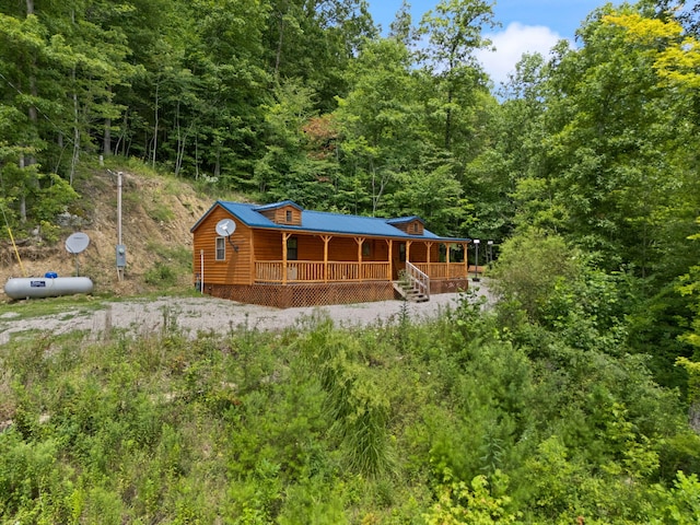 view of front of home with metal roof, a porch, and a forest view