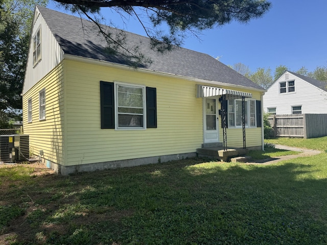 back of property with a yard, central air condition unit, a shingled roof, and fence