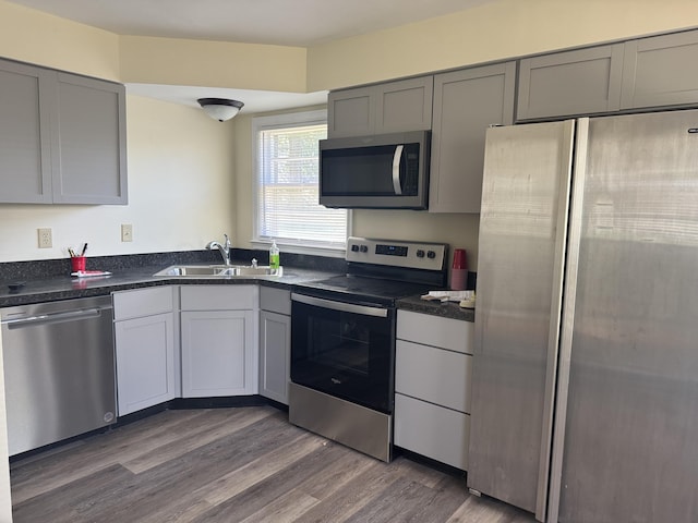 kitchen with dark countertops, a sink, gray cabinets, appliances with stainless steel finishes, and dark wood-style floors
