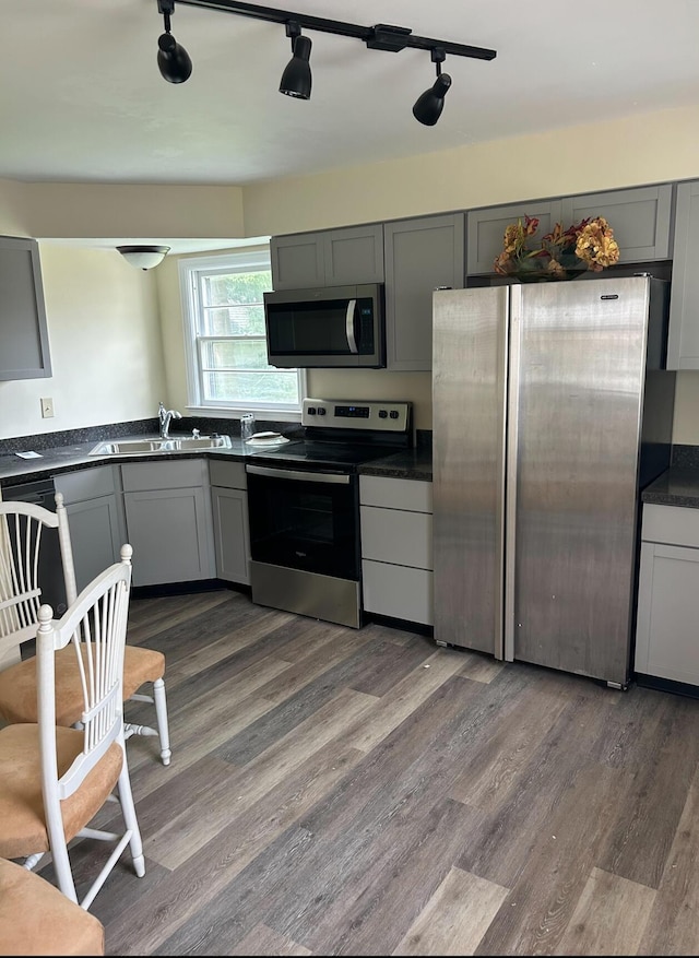 kitchen featuring stainless steel appliances, a sink, dark countertops, wood finished floors, and gray cabinetry