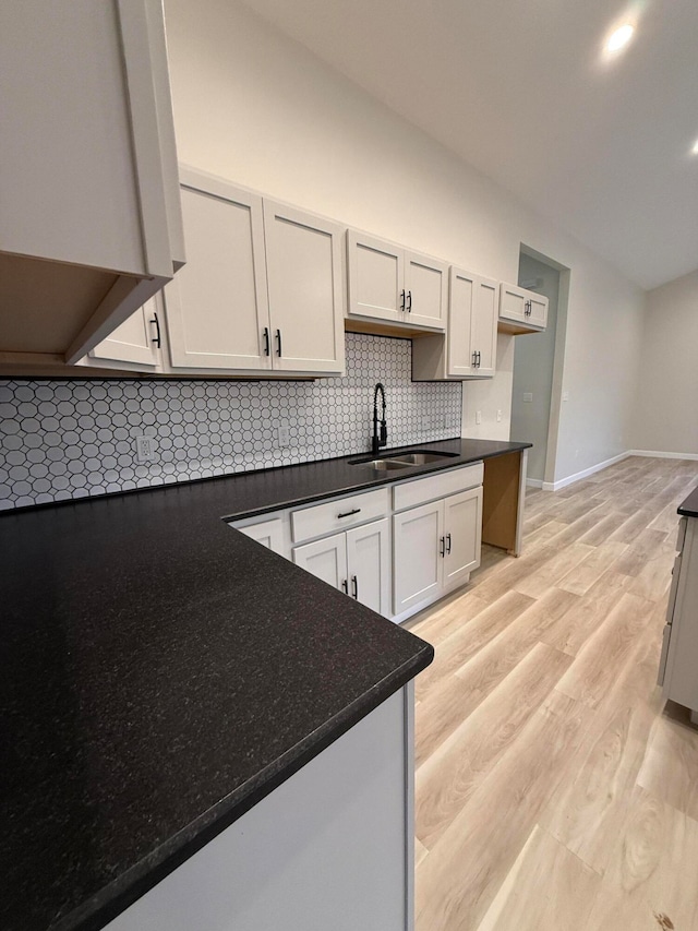 kitchen featuring baseboards, decorative backsplash, dark countertops, light wood-style flooring, and a sink