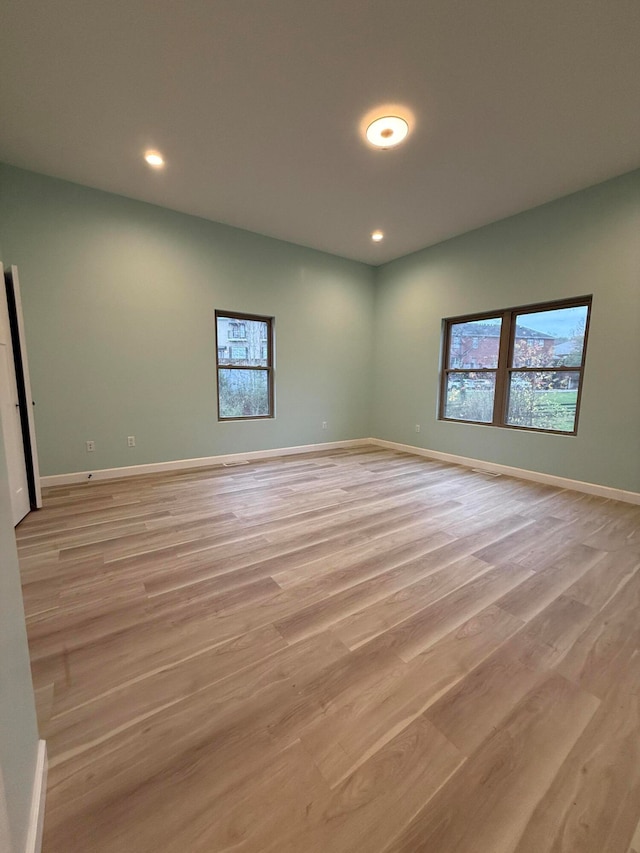 empty room featuring light wood-style floors, plenty of natural light, and baseboards