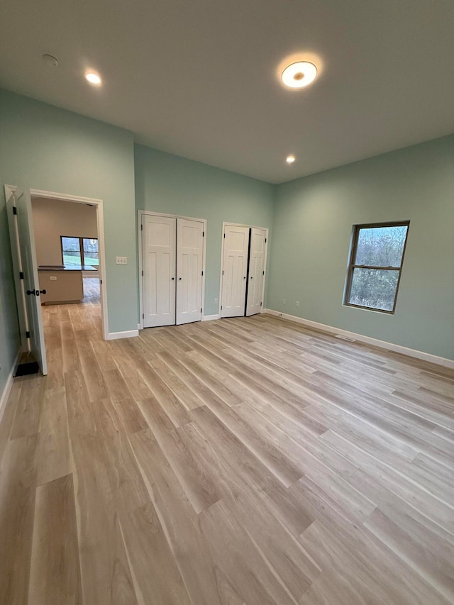 unfurnished bedroom with multiple closets, recessed lighting, light wood-style flooring, and baseboards