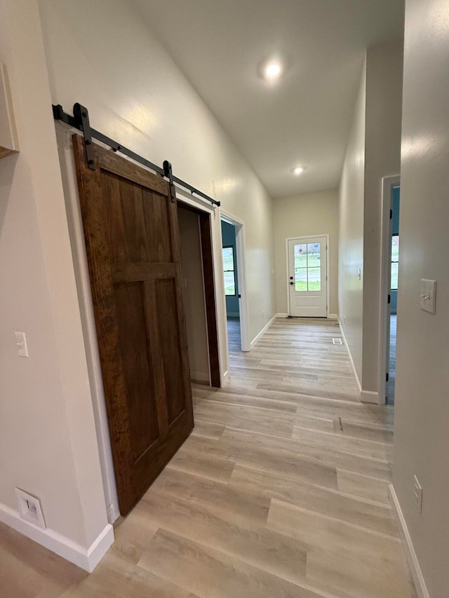 corridor with light wood-type flooring, a barn door, baseboards, and recessed lighting