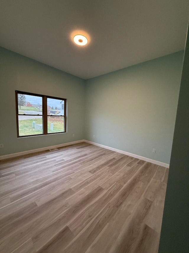 spare room with light wood finished floors, visible vents, and baseboards