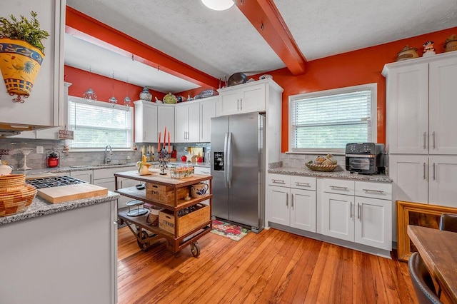 kitchen with decorative backsplash, beam ceiling, white cabinetry, and stainless steel fridge with ice dispenser