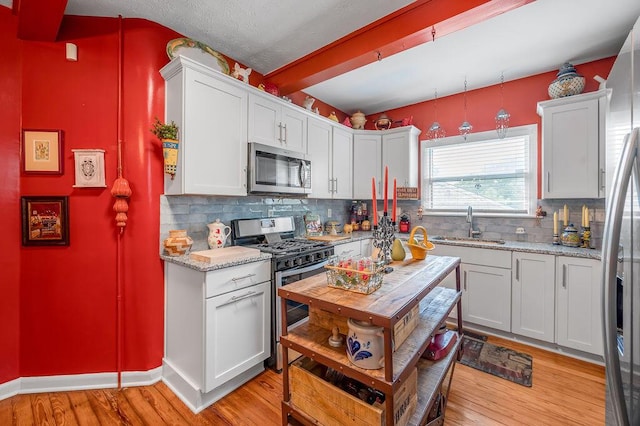 kitchen with stainless steel appliances, white cabinetry, a sink, and light stone counters