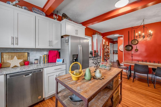 kitchen with stainless steel appliances, white cabinets, decorative light fixtures, and light stone counters