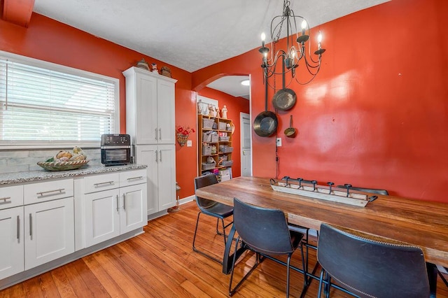 kitchen with arched walkways, white cabinets, hanging light fixtures, light wood-style floors, and a notable chandelier