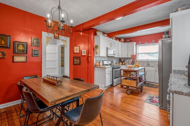 dining room with an inviting chandelier, light wood-style flooring, baseboards, and beamed ceiling