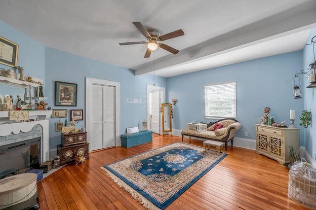 living area with a brick fireplace, light wood-style flooring, baseboards, and a ceiling fan