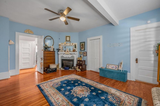 living area featuring ceiling fan, a fireplace, beamed ceiling, and wood finished floors