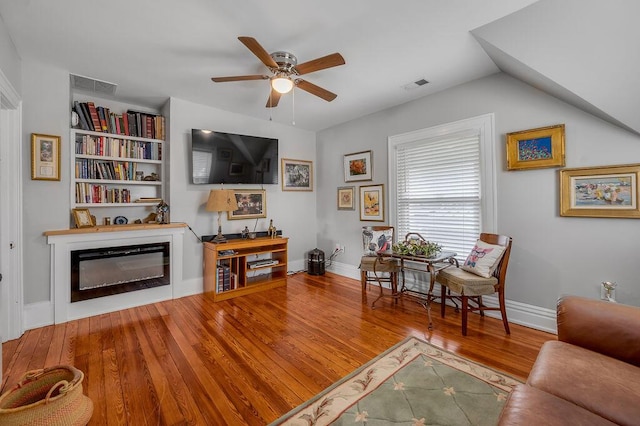 living area featuring a glass covered fireplace, wood finished floors, visible vents, and a ceiling fan