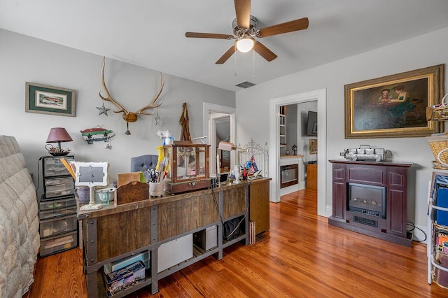 office space with ceiling fan, a glass covered fireplace, wood finished floors, and visible vents