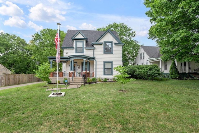 victorian home with covered porch, fence, and a front lawn