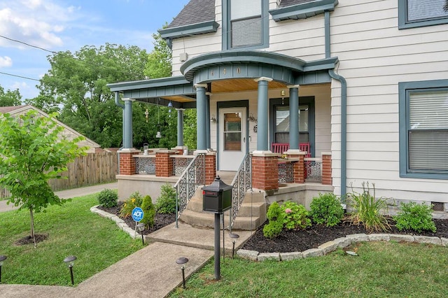 doorway to property with a porch, a lawn, a shingled roof, and fence