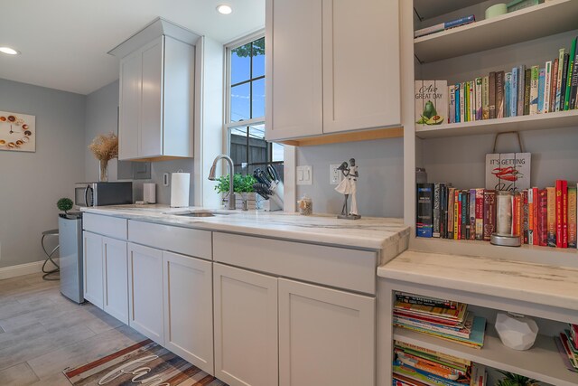 kitchen featuring white cabinets, light hardwood / wood-style floors, light stone counters, and sink