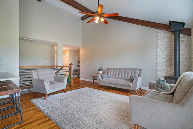 living room featuring beamed ceiling, a wood stove, wood-type flooring, and ceiling fan