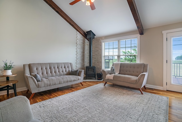 living room featuring light hardwood / wood-style flooring, a wood stove, beam ceiling, high vaulted ceiling, and ceiling fan