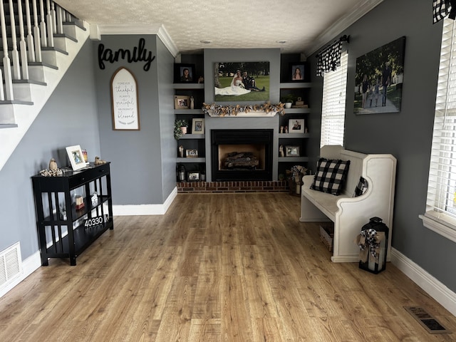 living area featuring built in shelves, crown molding, wood-type flooring, and a textured ceiling