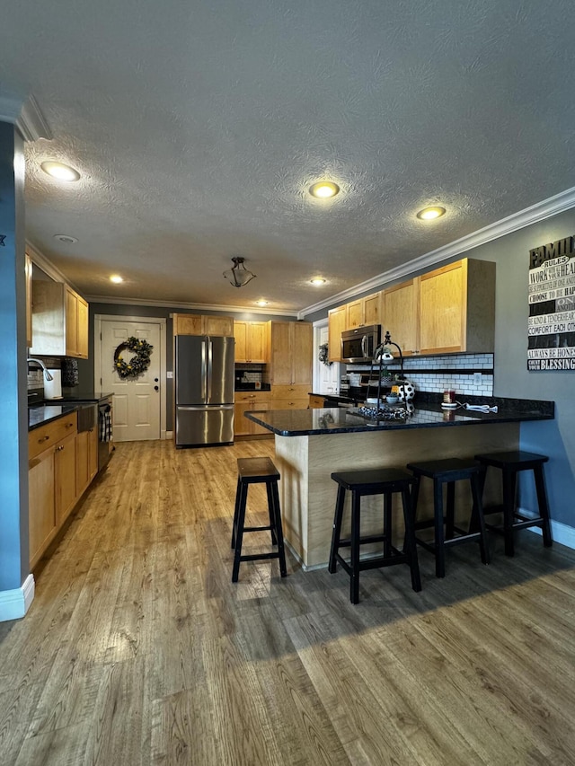 kitchen featuring kitchen peninsula, appliances with stainless steel finishes, a kitchen breakfast bar, crown molding, and hardwood / wood-style flooring