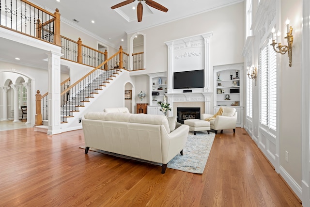 living area featuring stairs, a glass covered fireplace, a towering ceiling, and light wood-style floors