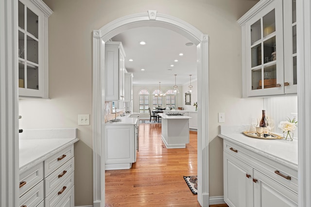 bar with light stone counters, white cabinetry, decorative light fixtures, and light wood-type flooring