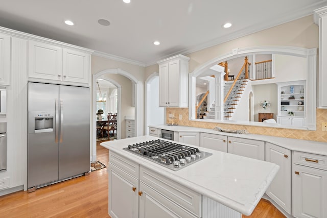 kitchen with appliances with stainless steel finishes, backsplash, light hardwood / wood-style floors, white cabinets, and crown molding