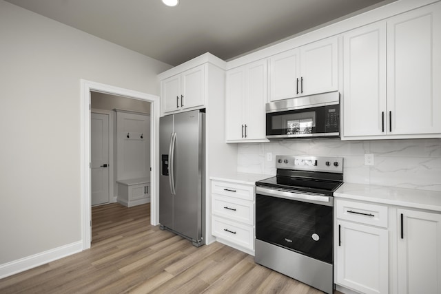 kitchen with white cabinetry, backsplash, stainless steel appliances, light stone countertops, and light hardwood / wood-style flooring