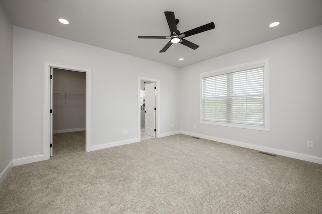 unfurnished bedroom featuring a spacious closet, light carpet, ceiling fan, and a closet