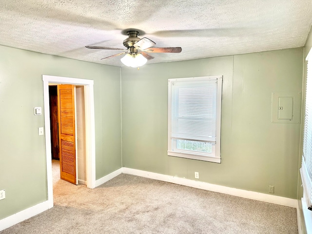 empty room with electric panel, light colored carpet, a textured ceiling, and ceiling fan