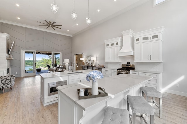 kitchen featuring a large island, sink, premium range hood, stainless steel gas range oven, and white cabinets