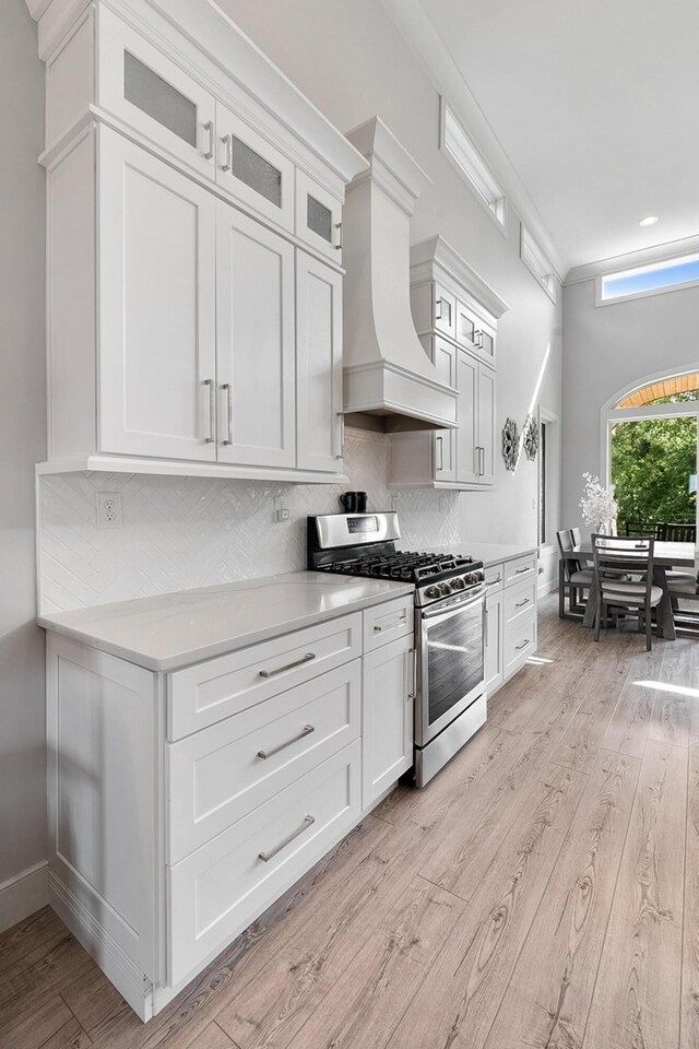 kitchen with tasteful backsplash, white cabinets, light hardwood / wood-style floors, custom exhaust hood, and stainless steel range with gas cooktop