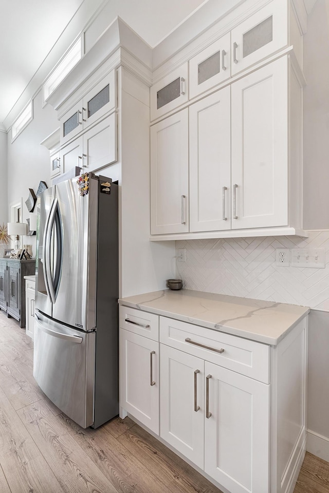 kitchen featuring stainless steel fridge with ice dispenser, white cabinets, decorative backsplash, light hardwood / wood-style floors, and light stone counters