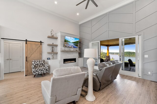 living room with crown molding, light wood-type flooring, a barn door, ceiling fan, and a tiled fireplace