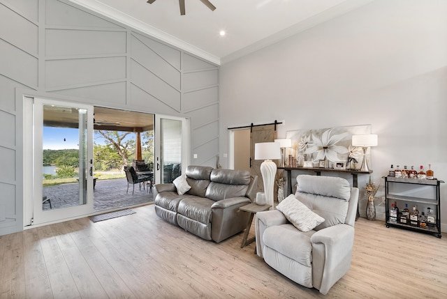 living room featuring a barn door, crown molding, light wood-type flooring, ceiling fan, and a towering ceiling