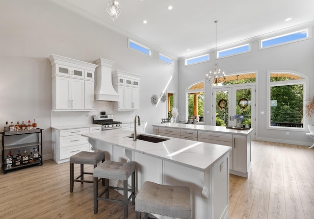 kitchen with custom exhaust hood, white cabinetry, sink, and a center island with sink