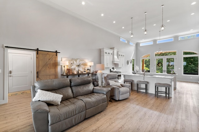 living room featuring a barn door, a chandelier, light wood-type flooring, and a towering ceiling