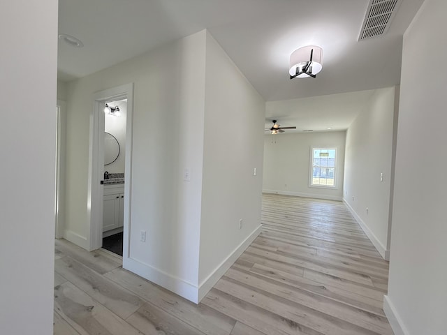 corridor featuring light wood-style flooring, baseboards, and visible vents