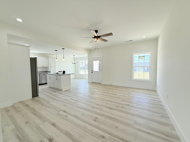 unfurnished living room with ceiling fan with notable chandelier, light hardwood / wood-style floors, and a wealth of natural light