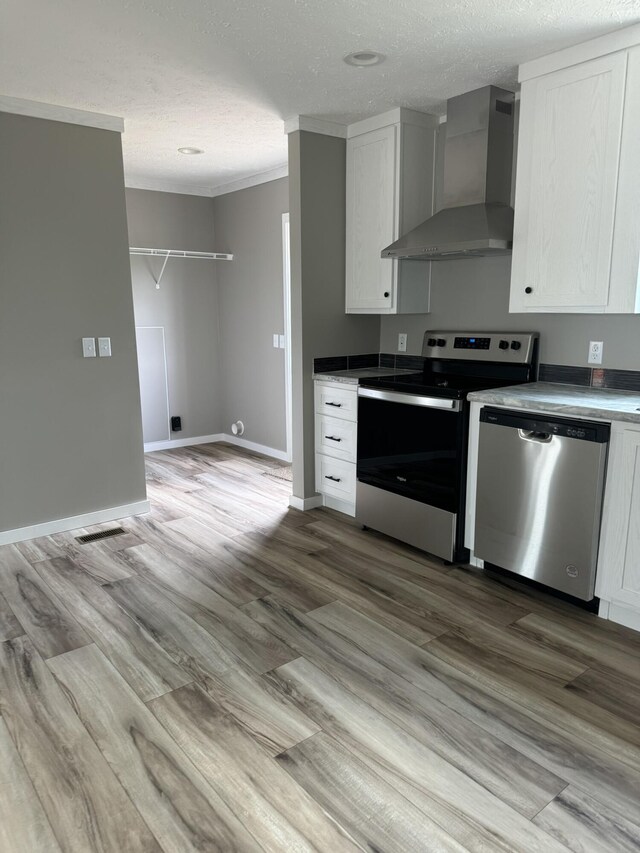 kitchen featuring hardwood / wood-style flooring, wall chimney range hood, stainless steel appliances, sink, and a textured ceiling