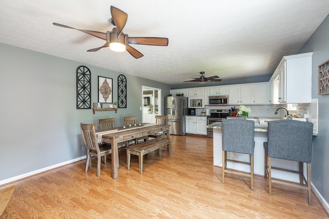 dining area featuring light wood-type flooring, a ceiling fan, baseboards, and a textured ceiling