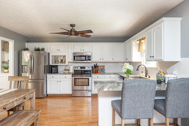 kitchen featuring a peninsula, appliances with stainless steel finishes, light wood-style flooring, and white cabinetry