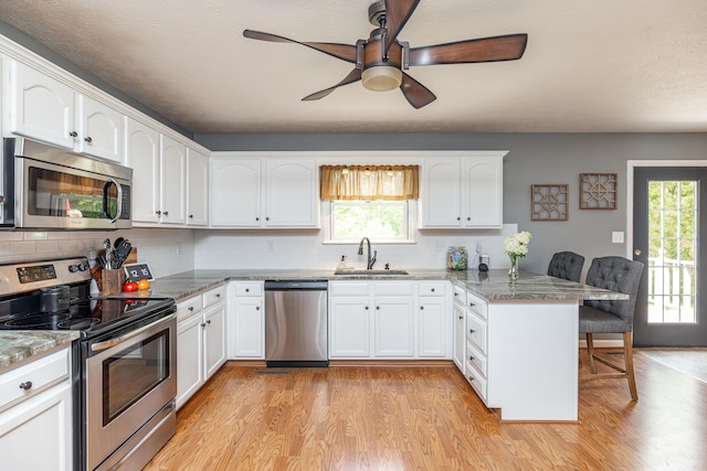 kitchen featuring a breakfast bar area, stainless steel appliances, a sink, light wood-type flooring, and a peninsula