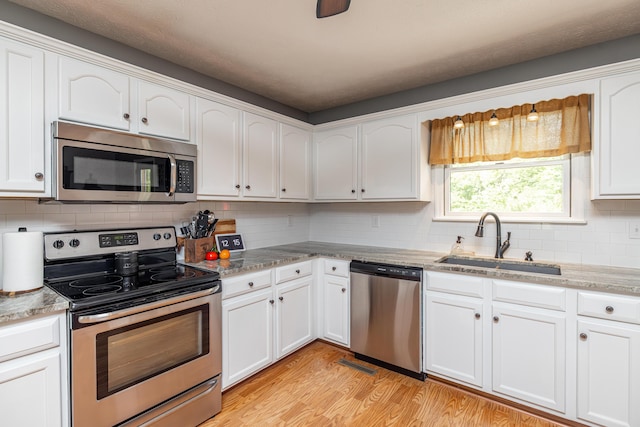 kitchen with stainless steel appliances, decorative backsplash, white cabinetry, a sink, and light wood-type flooring